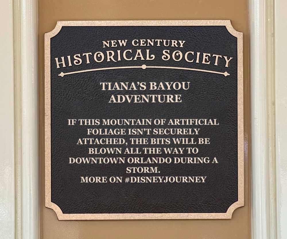 A photo of a plaque doctored to read, "New Century Historical Society. Tiana's Bayou Adventure. If this mountain of artificial foliage isn't securely attached, the bits will be blown all the way to downtown Orlando during a storm. More on #DisneyJourney"