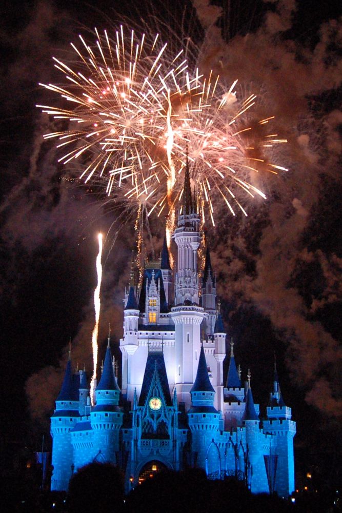 Photo of fireworks exploding above Cinderella Castle lit with white and blue lights.