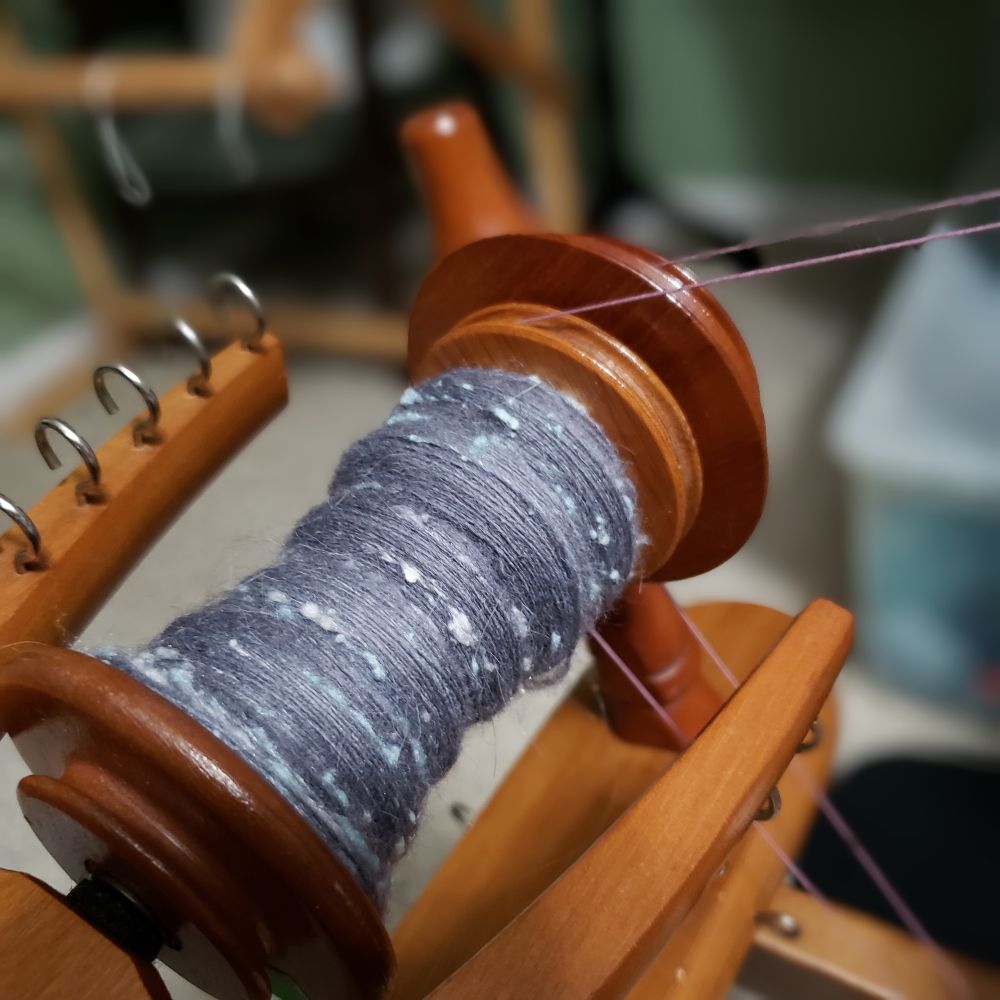 Yesterday's Tour de Fleece progress. A closeup view of Kelli's Ashford Traditional spinning wheel. The bobbin is partially full of handspun singles that are primarily medium dark grey targhee wool and llama fiber along with pale silver grey and pastel blue silk noil. 
