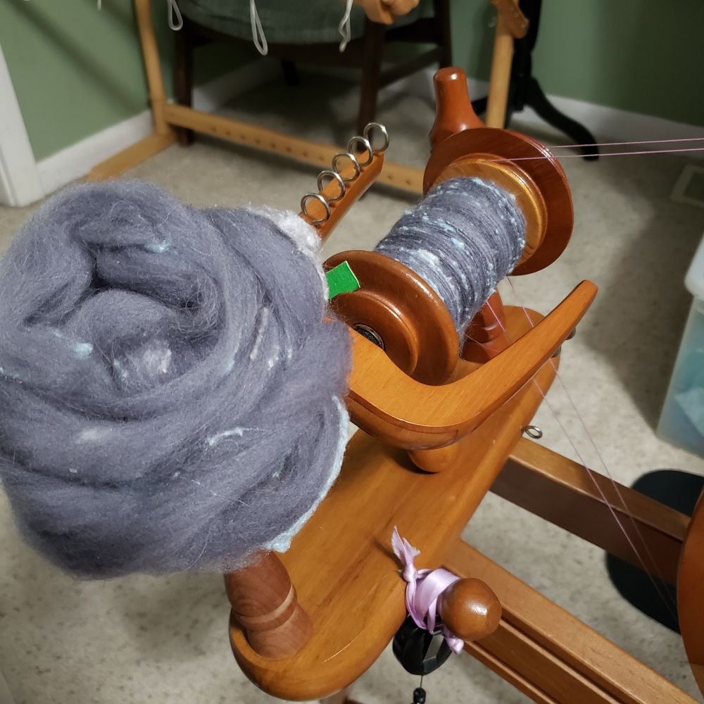 Today's Tour de Fleece progress. A closeup view of Kelli's Ashford Traditional spinning wheel. The bobbin is mostly full of handspun singles that are primarily medium dark grey targhee wool and llama fiber along with pale silver grey and pastel blue silk noil. The fiber nest that sits on top of the front maiden upright is all that is left to spin.