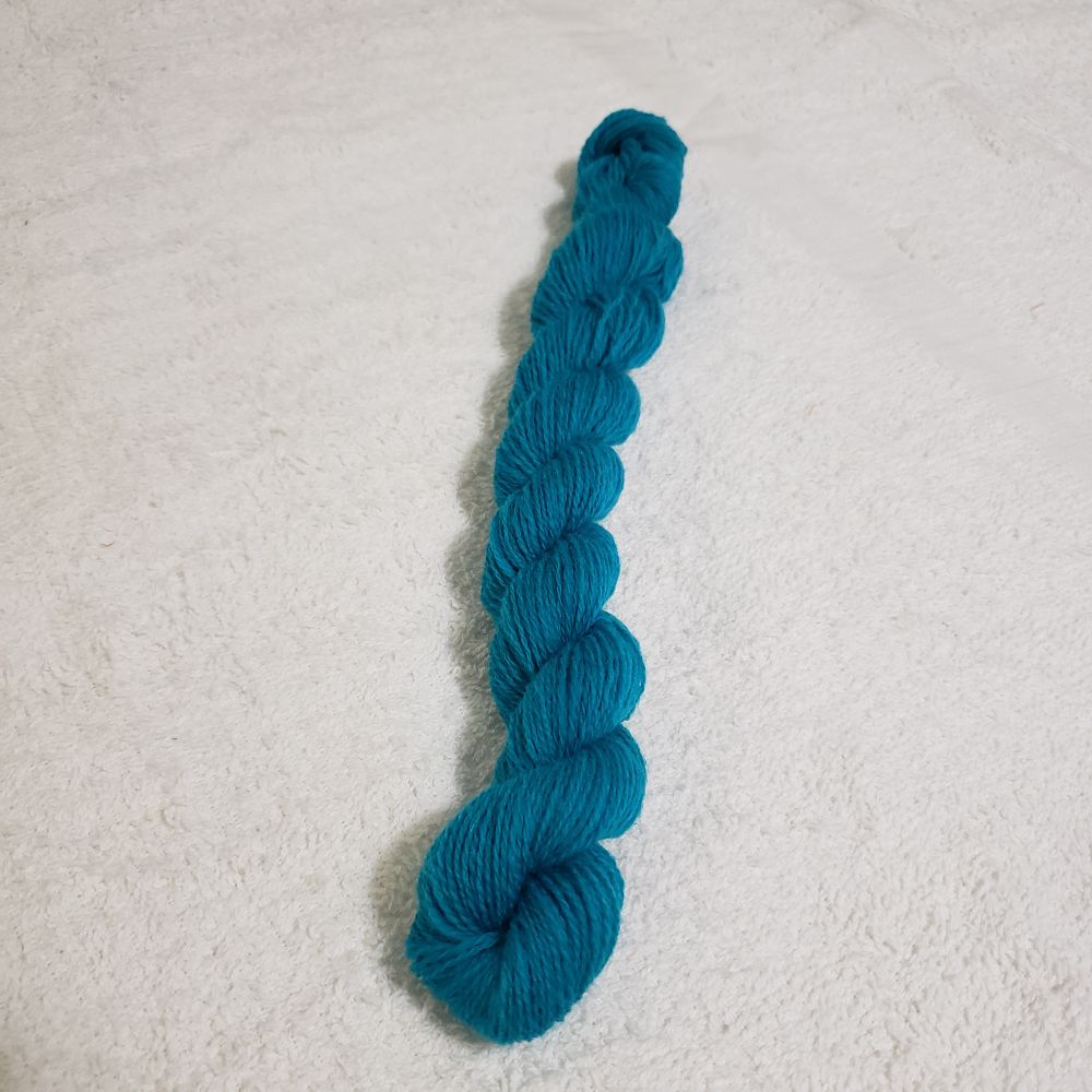 A small skein of turquoise superwash merino wool two ply handspun yarn sits on top of a white terrycloth towel.