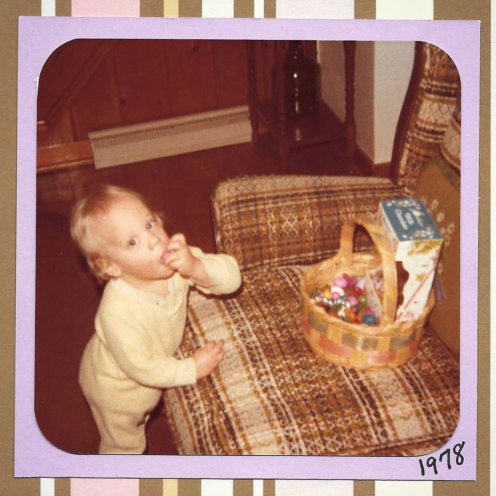 An aged passport from 1978 showing a small child standing next to a sofa, an Easter basket on the seat. He is stuffing his face with candy and looking at the camera. 