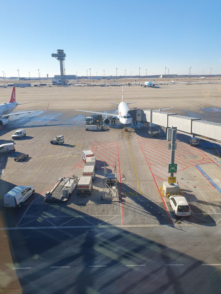 View from an airport terminal looking at the plane waiting to board passengers. Airfield and airport tower in the background