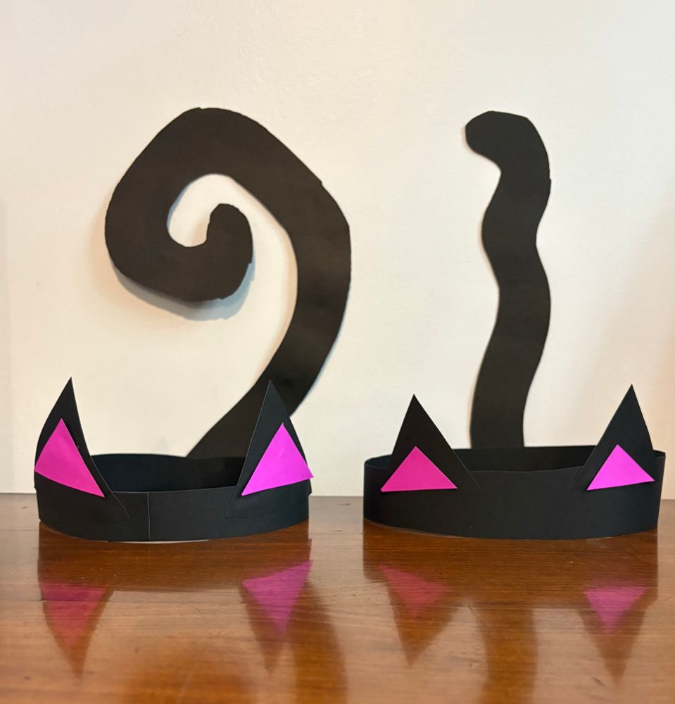Two black headbands made from construction paper with black cat ears. Behind them hang two black cat tails. 