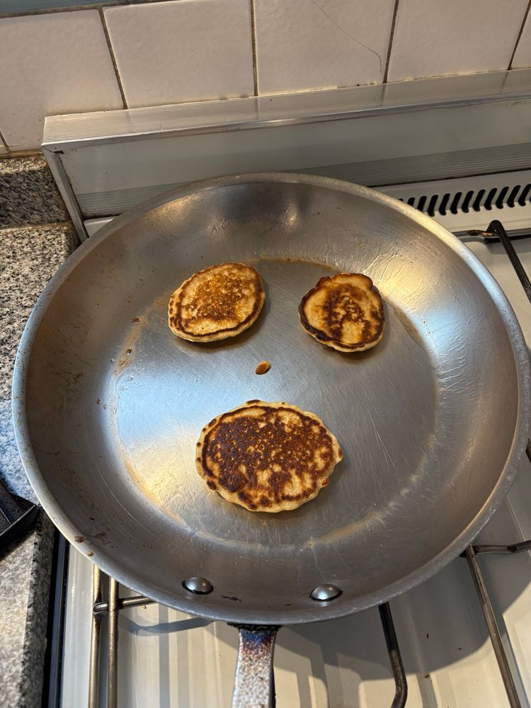 Three small pancakes and a pancake fleck in a stainless steak pan making a screaming face. 