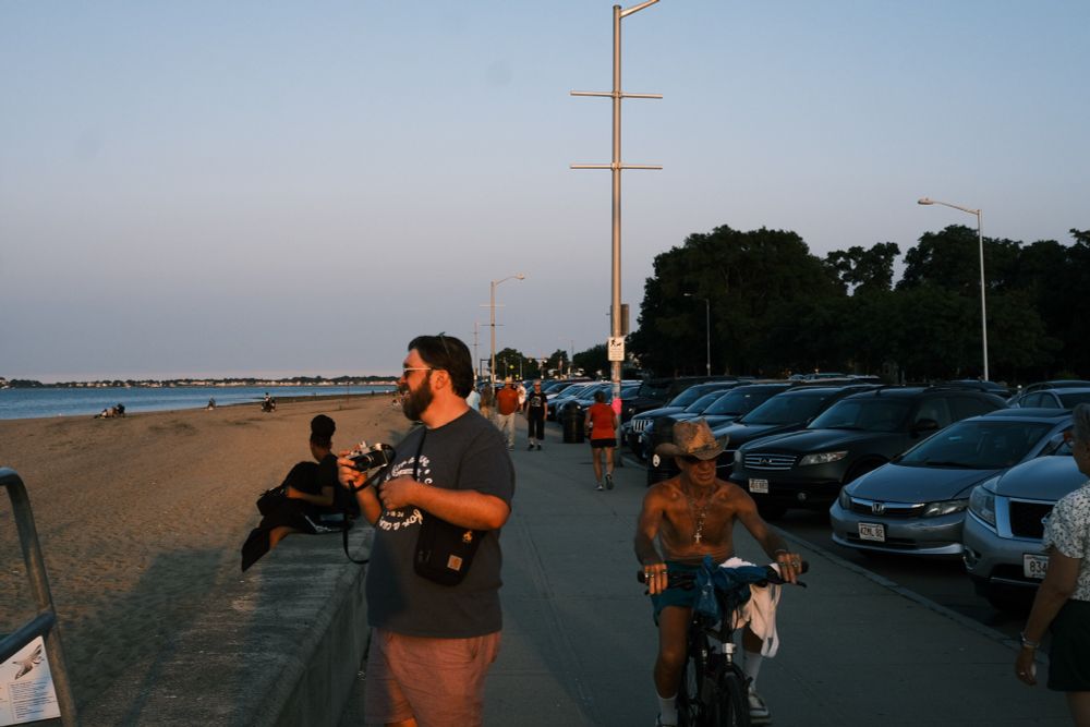 Golden hour photo of me, a large white giy in glasses, holding a camera while a shirtless man in a cowboy hat rides by