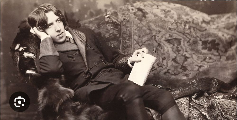 Young man in a smoking jacket and breeches semi reclining on a fur covered couch, with his head resting on his hand. A book held idly in the other hand.