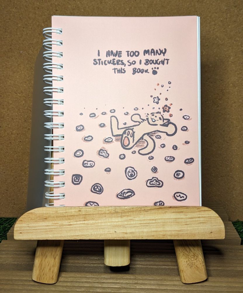 an a6 sized sticker book featuring a cat laying down surrounded by stickers. the top of the book reads, "I have too many stickers, so I bought this book" with a pawprint beside it! 