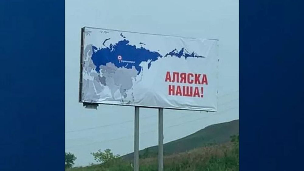 A sign in ruzzia with a blue map on white background of ruzzia and Alaska to its East, with the words "Alaska is ours!" in ruzzian