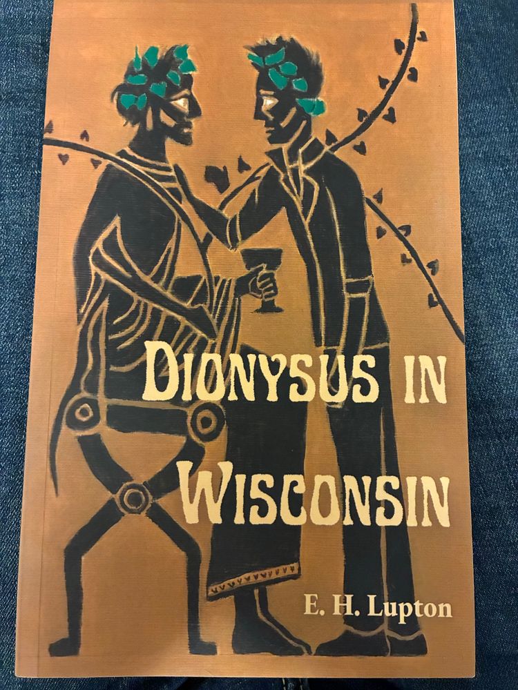 A book. Dionysus in Wisconsin. E.H. Lupton. A bronze cover with black etching- look figures of two men wearing green ivy wreaths. One is sitting down holding a goblet and the other leans towards him with a hand on his shoulder. 