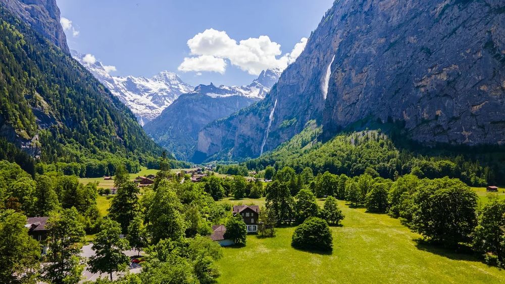 Lauterbrunnen in Switzerland — a view down a lovely valley with steep walls. Waterfalls are cascading down the walls and in the distance, at the end of the valley, you see snow-capped Alps.
