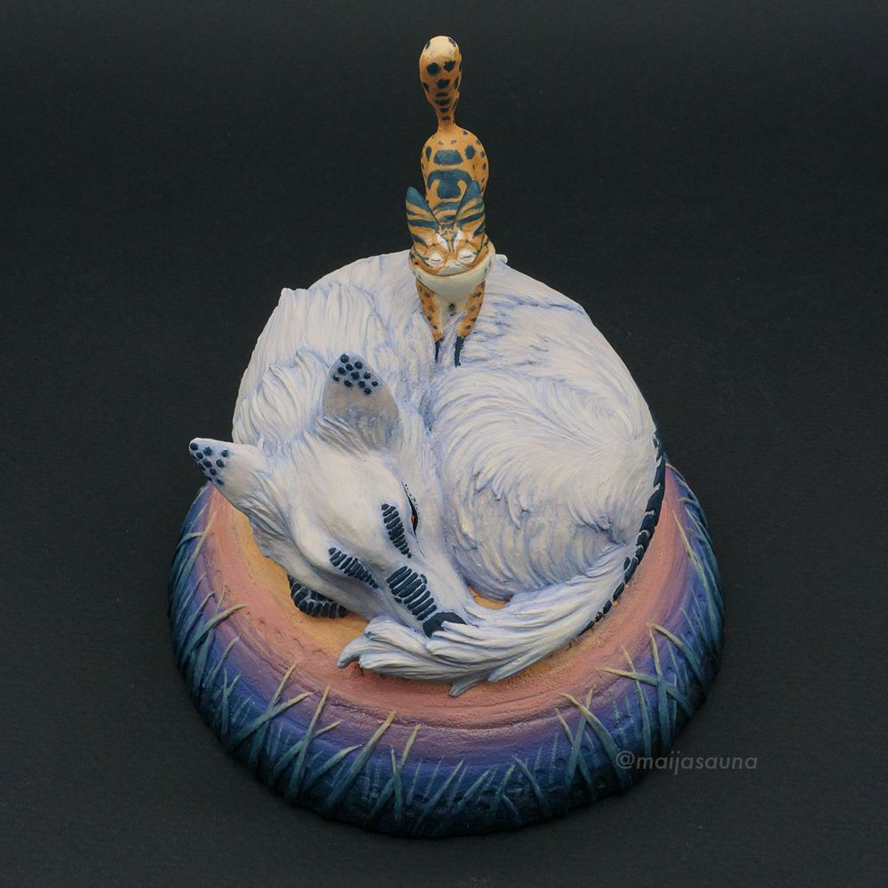 A small (coffee-cup-size) sculpture of an star wars cat creature kneading the fur of a snoozing wolf creature both from the Star Wars world of Lothal. The white Loth-wolf is curled up into a sleepy doughnut with its floofy tail over its nose. Loth-cat is doing a Big Stretch. The cat has a goofy ball of a head with two conical ears, skinny stick legs, and its puffy tail stands straight up with happiness.