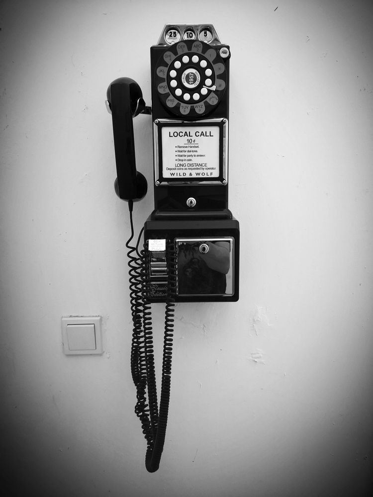 Ein altes, amerikanisches Münztelefon mit Wählscheibe an einer Wand.