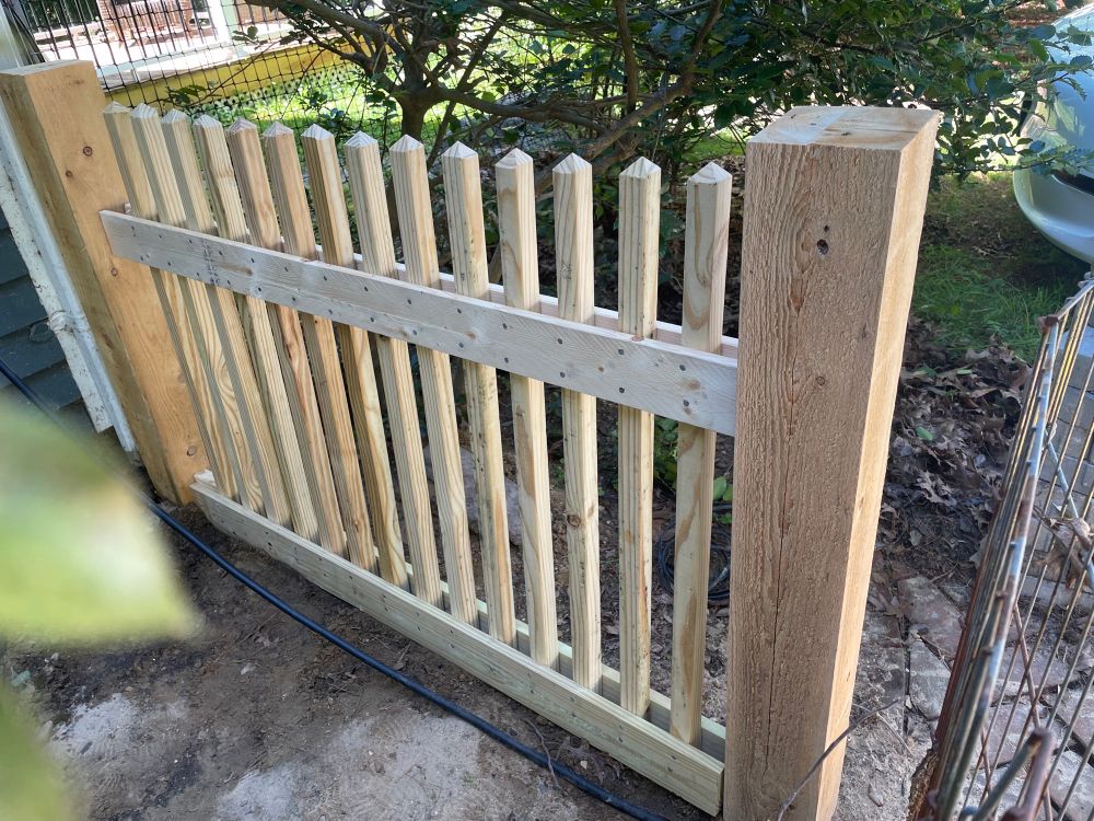 A pressure treated wood picket fence with pointy tipped pickets 