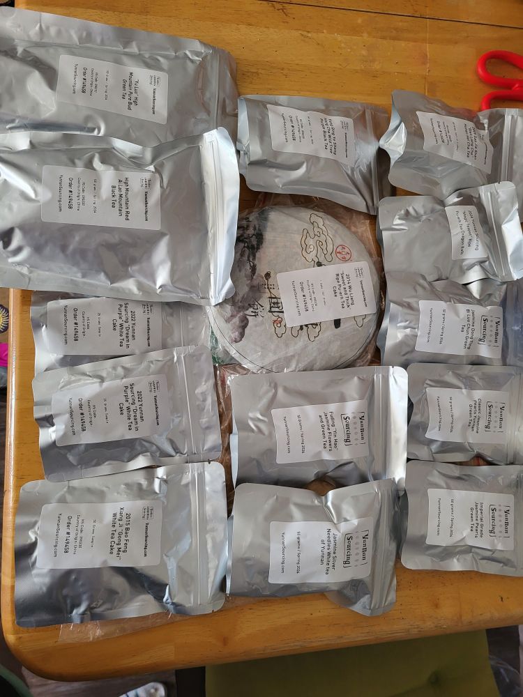 A bing of tea and several silver bags of various loose leaf teas, arranged together on a table.