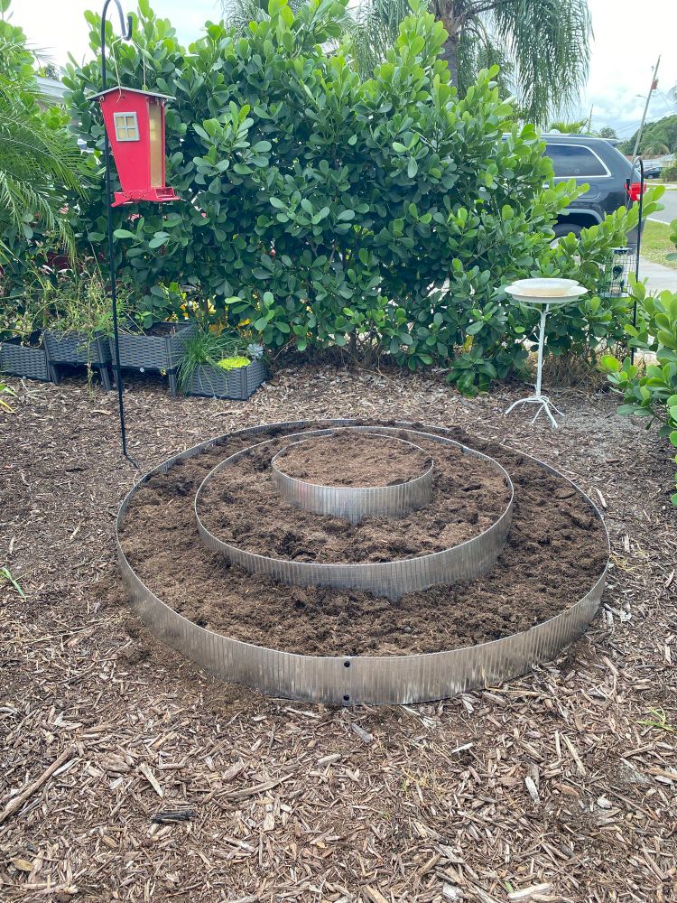 Round garden filled with dirt and surrounded with bird bath and feeders