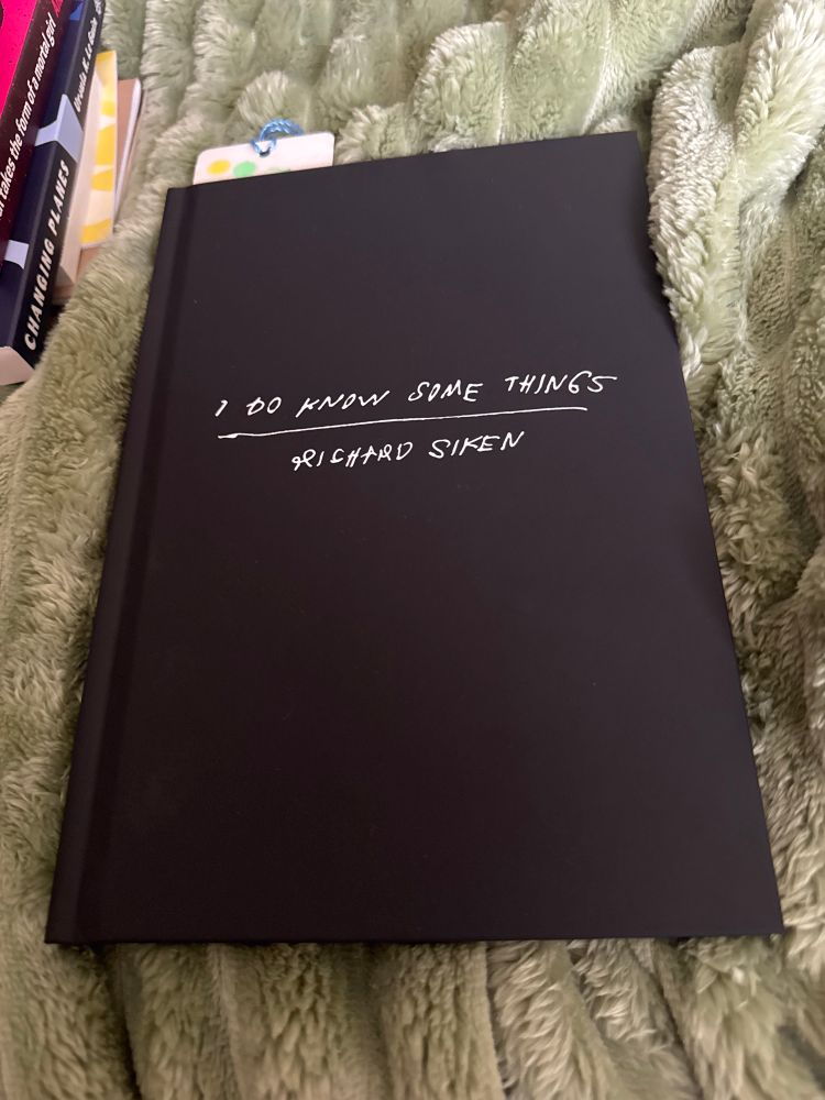 Picture of an all black hardcover book with the title, “I Do Know Some Things”, and the authors name, Richard Siken, written in white font that resembles hand writing. The book is sitting on a textured sage green blanket.