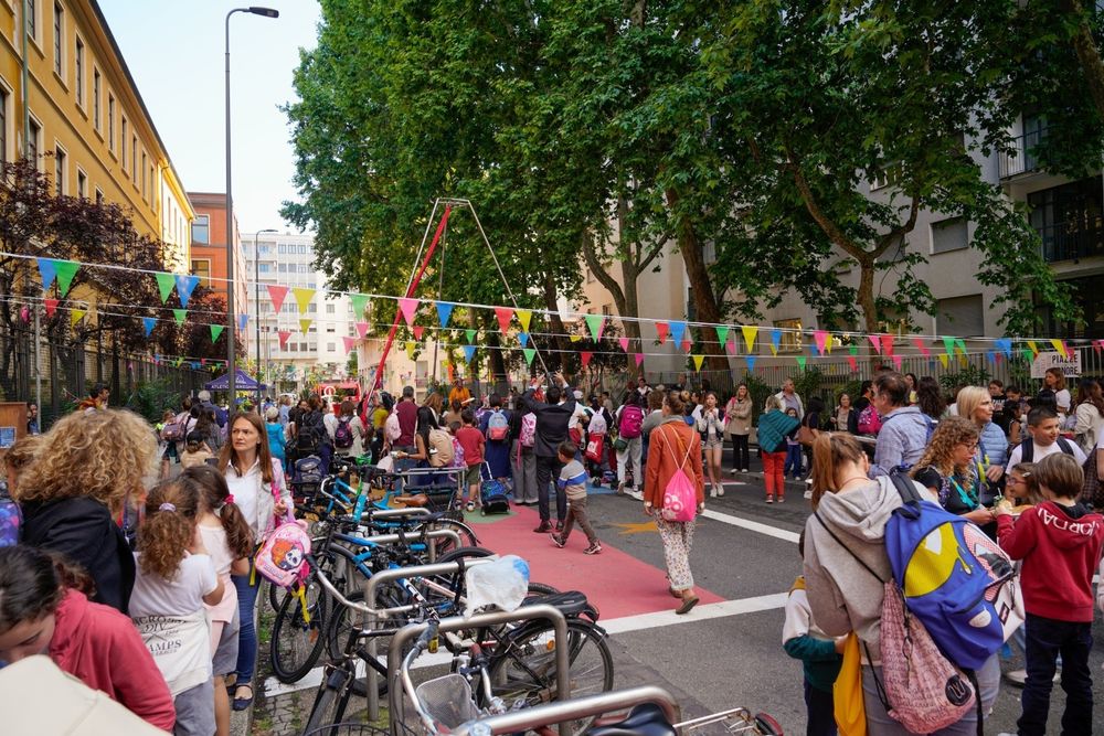 a picture of the same street which is now pedestrianized with bike parking, colorful designs on the ground, bunting and a lot of children and adults 