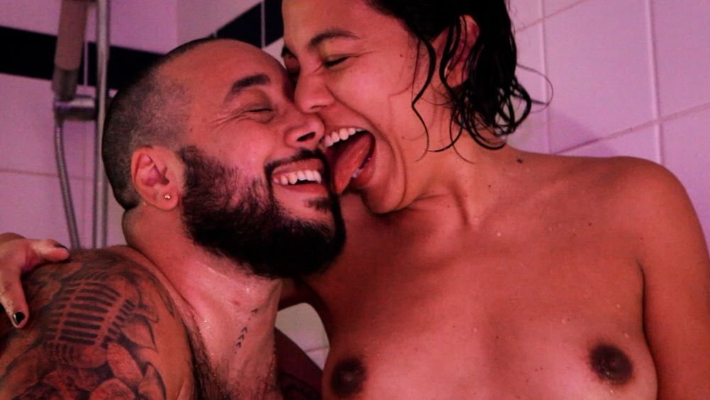 Queer brown porn performer couple Robin Astera and Lina Bembe laugh and hug in a shower.