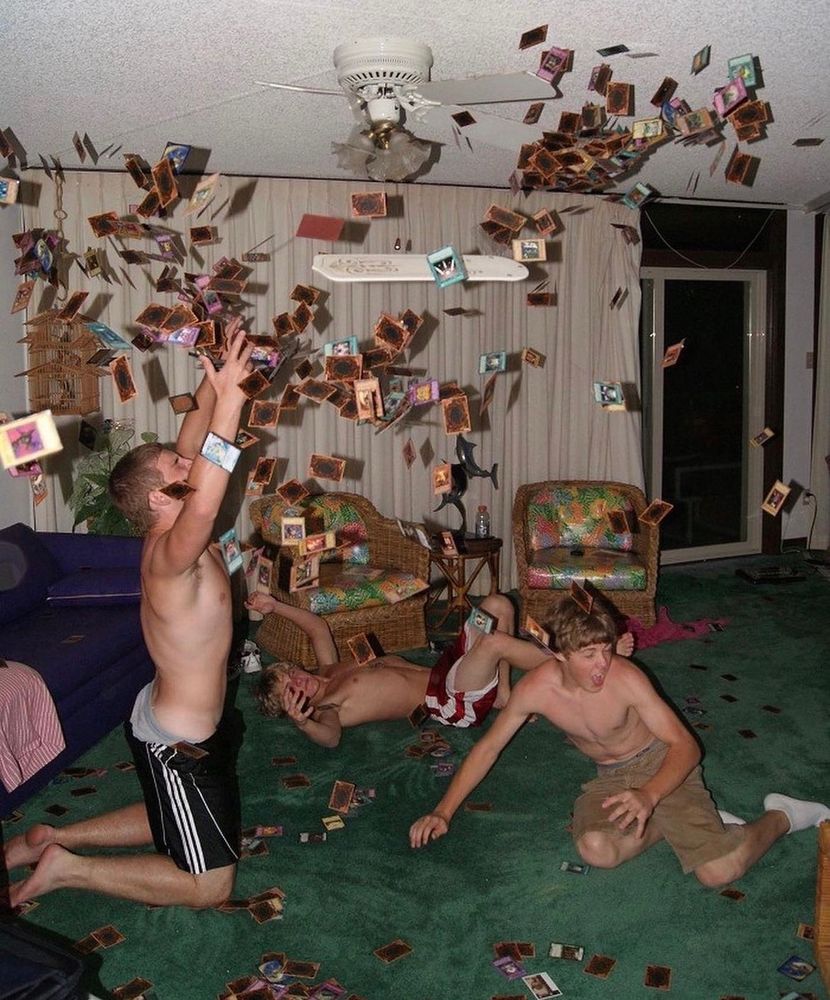 A picture from the early 2000's showing three shirtless fellas attempting to collect a cloud of falling Yu-Gi-Oh cards 