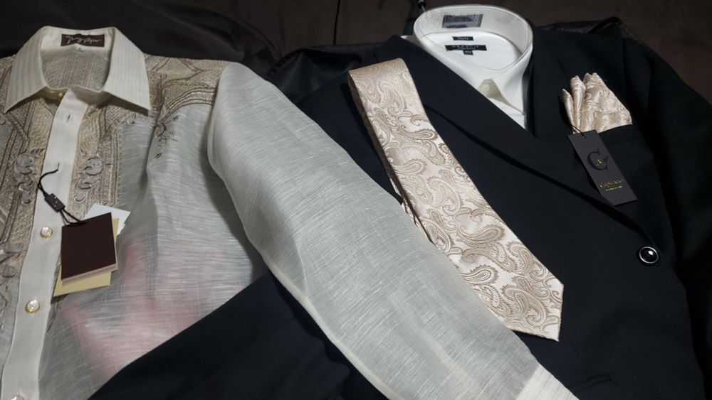A barong filipino next to a formal black suit. The suit's tie and pocket cloth are cream paisley, matching the embroidered feel of the barong.