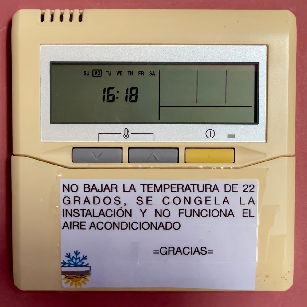 Control del aparato de aire acondicionado que dice: “NO BAJAR LA TEMPERATURA DE 22 GRADOS, SE CONGELA LA INSTALACIÓN Y NO FUNCIONA EL AIRE ACONDICIONADO. GRACIAS”