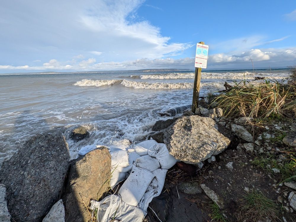 Waves rushing up against sandbags on a beach. 