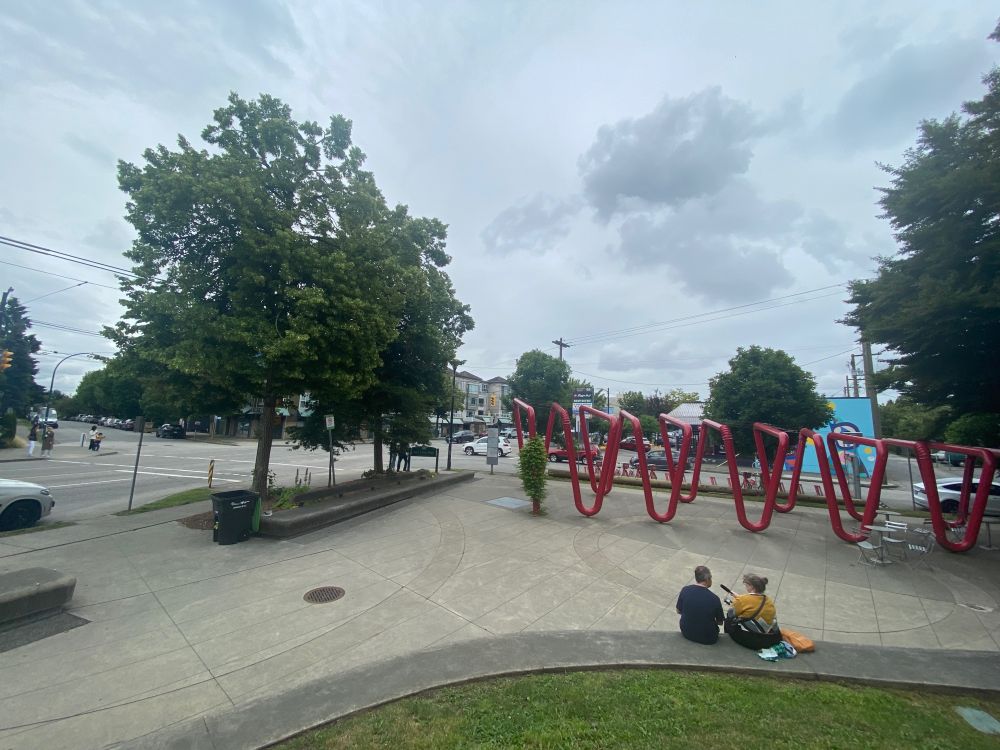 in Vancouver's tiny Sun Hop Park on the busy intersection of two streets, Helen Zaltzman and Justin McElroy sit recording on a low wall at the edge of a small grassy hillock. The rest of the park is paved, with an installation of giant red bendy straws forming a pergola