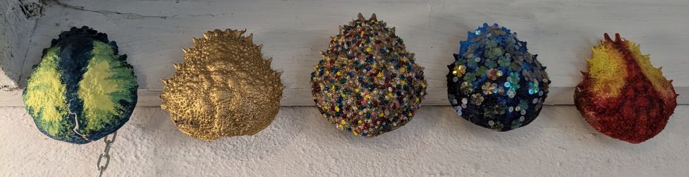 Five spider crab shells in a row all painted with different effects.