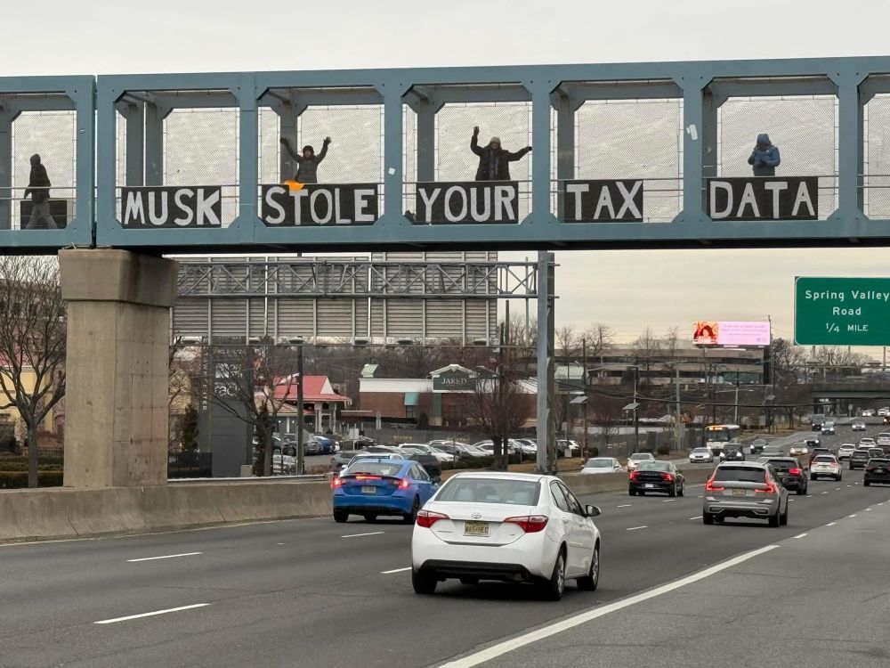 Photo of highway in NJ with signage “Musk stole your tax data” on pedestrian overpass.