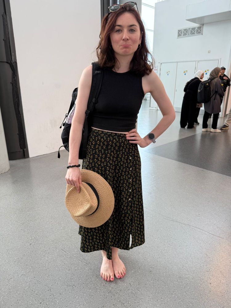 A shoeless woman pulling a sad face holing a holiday hat 