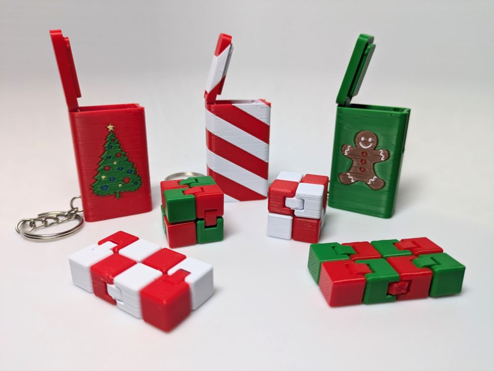 Picture of three Christmas themed snap boxes with fidget cubes. One is red and has a christmas tree, one is green with a gingerbread man, and the third is red and white stripes like a candy cane.