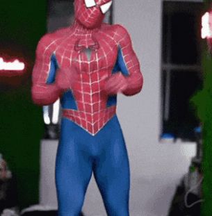 a man in a spiderman costume is dancing in front of a green wall .