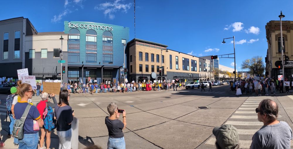 A view of a downtown area with people holding protest signs filling the sidewalks
