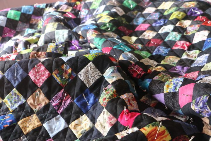 A nearly completely sewn quilt bunched up in a pile.  All the safety pins are ready to be removed, but it they hurt my fingers, so I have to take this part of the quilt making process slowly.