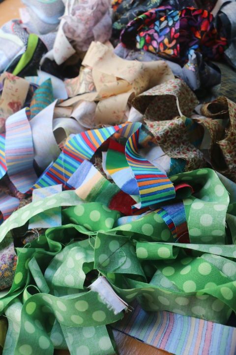 A pile of assorted fabrics cut into thin strips. They have been sewn together diagonally at the ends to create 1.8 metre lengths.