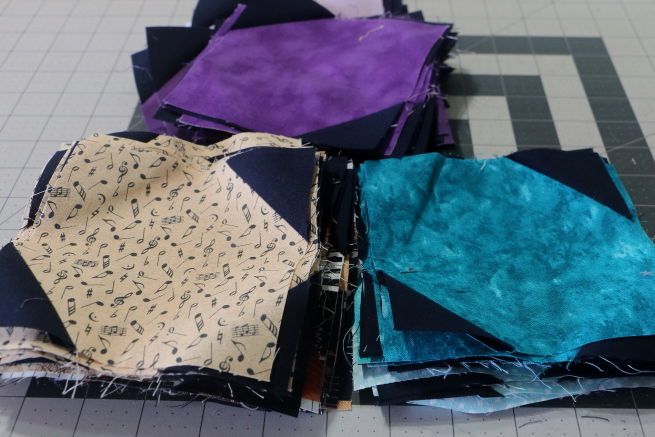 Half snowball fabric blocks made up of purple, turquoise, and brown music themed fabric.  The dark blue triangles have been pressed to the corners of the larger fabric squares.  Tomorrow, I put them on the design wall and see what happens.  Exciting!