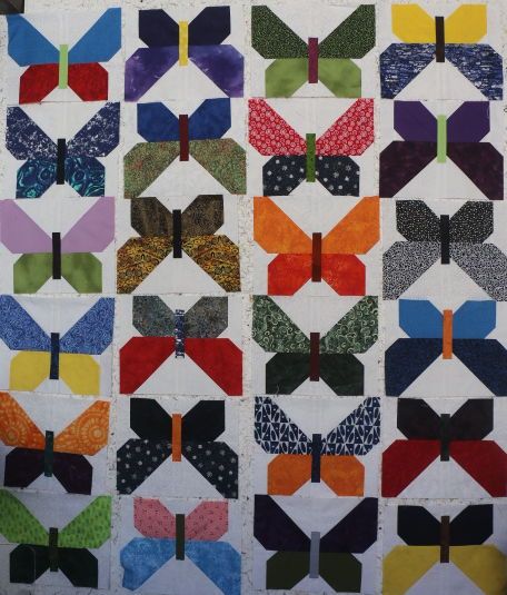 24 different butterfly quilt blocks on a design wall laid out in a 4 x 6 grid. Columns 1 and 3 have butterflies in a upwards direction. Columns 2 and 4 have rotated blocks 180 degrees so the butterflies are in a downwards direction.