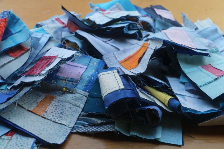 A pile of assorted blue fabrics sewn into squares.  A contrast colour is also sewn into the squares.