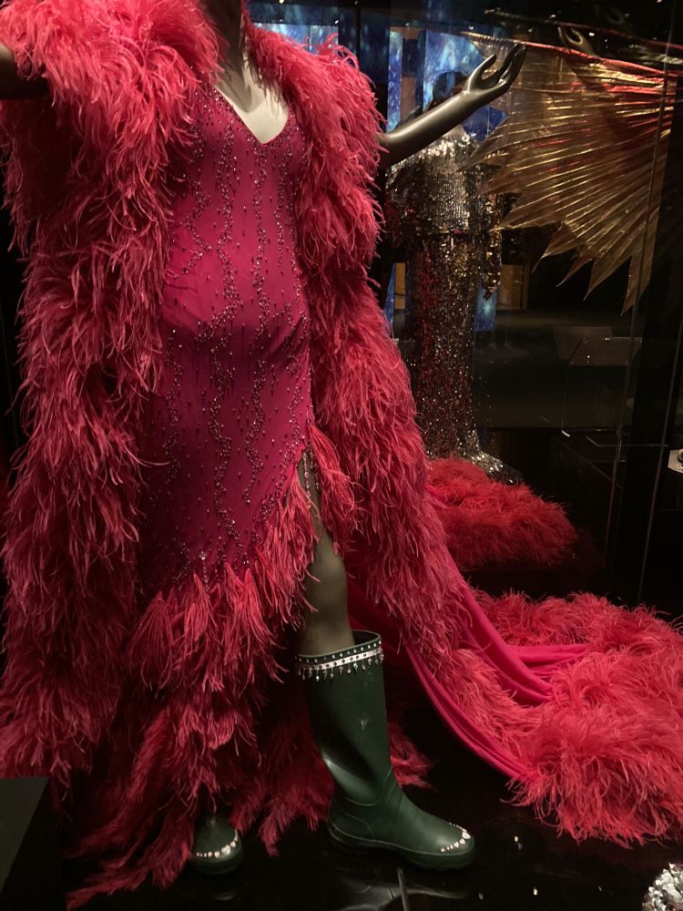 Red beaded full length dress with ostrich feathers, and bejewelled gumboots.