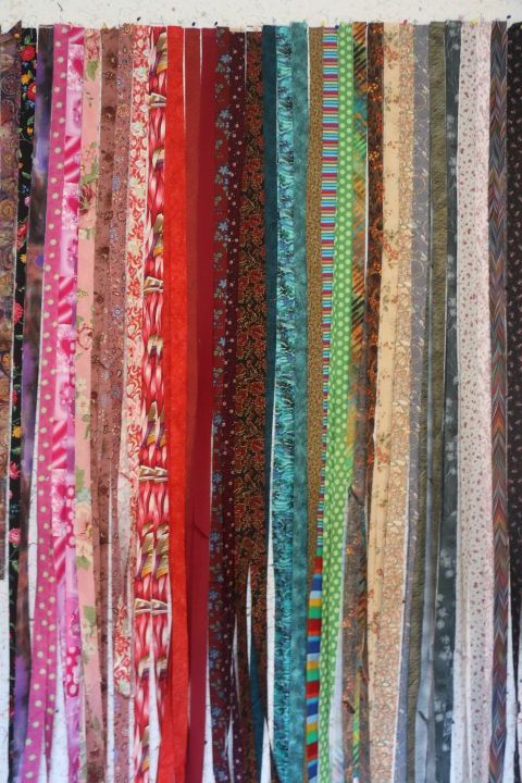 Colourful strips of fabric pinned to a design wall in sort of colour families, but I just wanted to see what fabric I had, and if the process would work with the binding tool. It has, so I can start making the binding. It works best if you make and iron it at the same time, then sew it to the fabric. If the crease gets left for a few hours, the crease unfolds too much for my liking.
