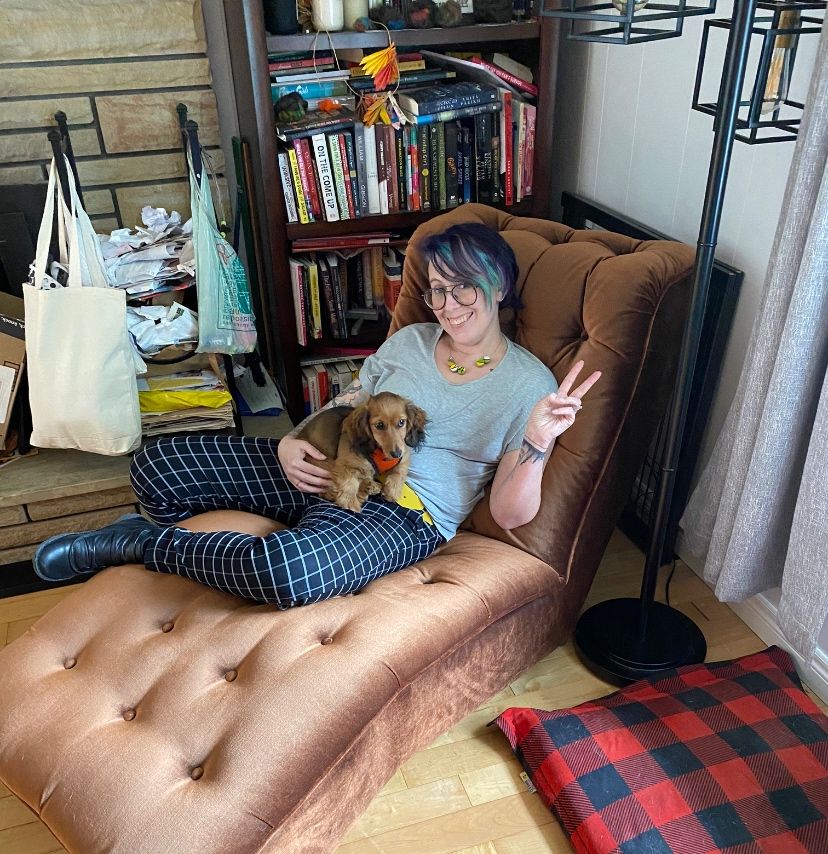 Potato (an adorable long-haired mini dachshund) and me, demonstrating the sheer vintage cool of a brown MCM-style chaise lounge by sitting on it awkwardly because I didn't want to put my shoes on the chair. There is a ridiculously stuffed bookshelf behind us and also a bunch of paperword we needed to burn back there too. 