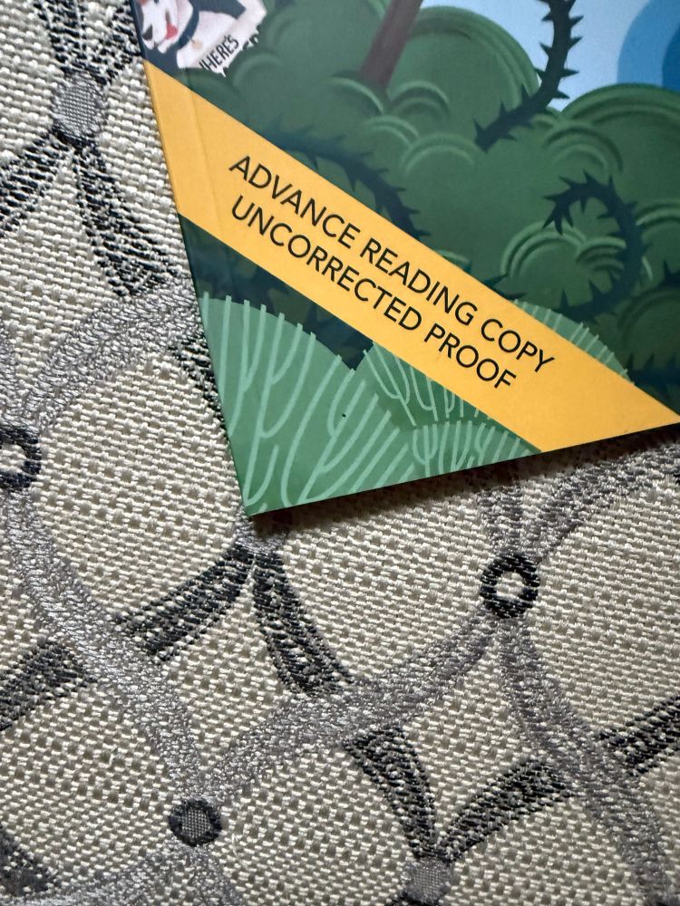 The corner of a book laying on upholstery. Shows leaves and vines and part of a dog, and has a banner across it that reads “Advance Reading Copy Uncorrected Proof” 