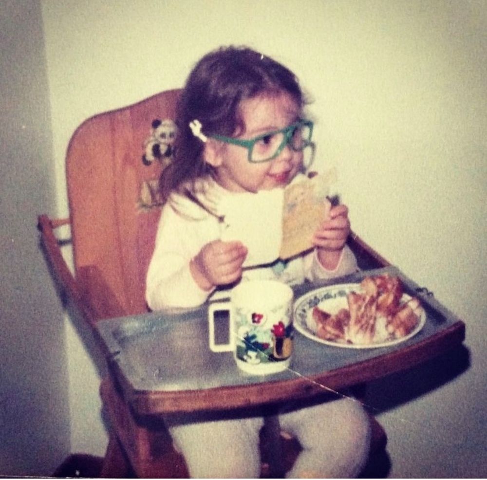 Lil Sal wearing big green glasses while reading a card in a high chair and absolutely annihilating a grilled cheese.