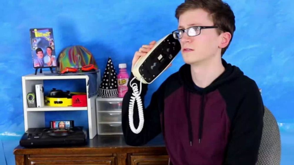 a boy wearing glasses is talking on a telephone in front of a blue wall