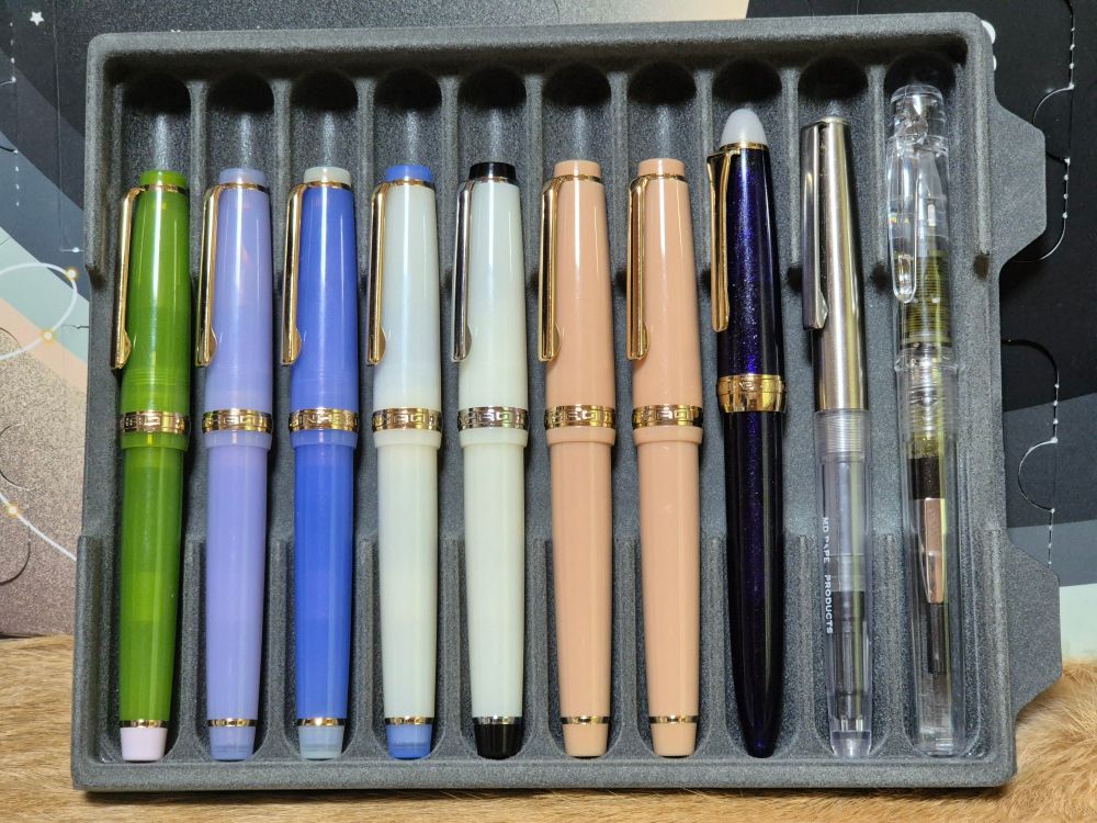 플라스틱 만년필 케이스에 만년필이 칸마다 채워져있다.
왼쪽부터 진하오82 미니 아보카도색, 연보라색, 청금석색, 반투명 흰색, 반투명 흰색, 밀크티색, 밀크티색, 세일러 시키오리 달밤의 수면 요나가, 미도리 만년필, 플래티넘 프레피 크리스탈색 만년필이 있다.