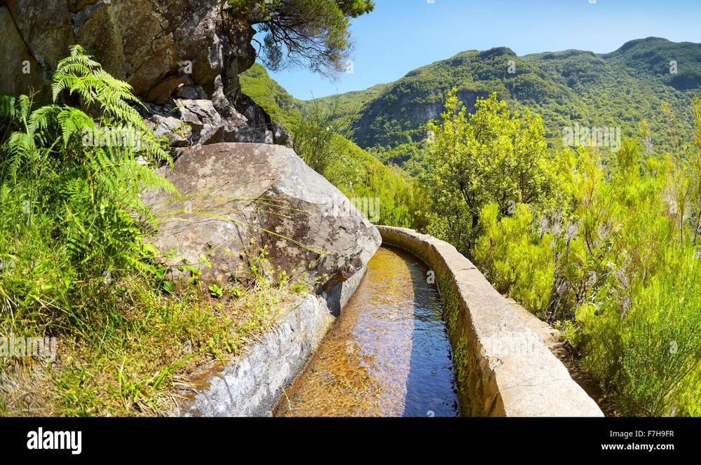 A narrow stone path with a drop off a mountainside and running water on the other