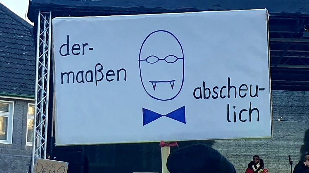 Schild aud einer Demo gegen Rechts.
Weisser Hintergrund auf dem ein Ei mit einer Fliege ( dem Kleidungsstück nicht dem Insekt ) und einer Brille mit kleinen runden Gläsern. Ein Mund ist als Strich mit Vampirzähnen angebracht. 
Der Text auf dem Schild lautet: 
Der - maaßen abscheulich