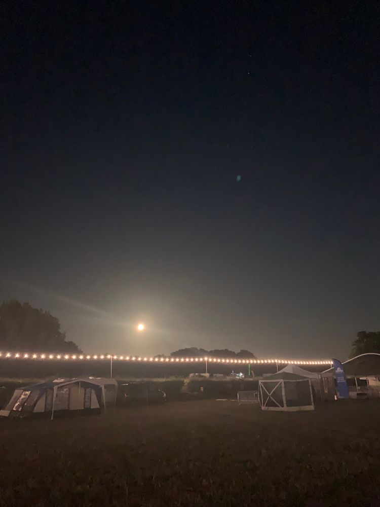 The bright Sturgeon Moon above the campsite at night. A lit row of bulb lights are strung along the campsite road.
