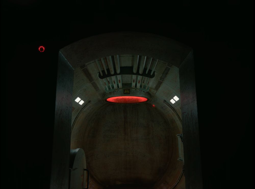 ominous interior - a tubular space that looks like the inside of a Soviet spaceship. dingy with graffiti all over the walls, and an orange-red hellish circular light at the top. in the foreground there's an archway and darkness on either side of it 